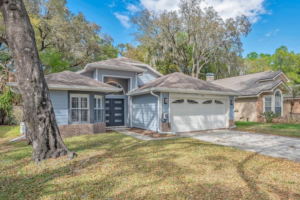 A light blue single-story house with a two-car garage and a large tree in front — 1001 PIEDMONT OAKS DRIVE, APOPKA, FL