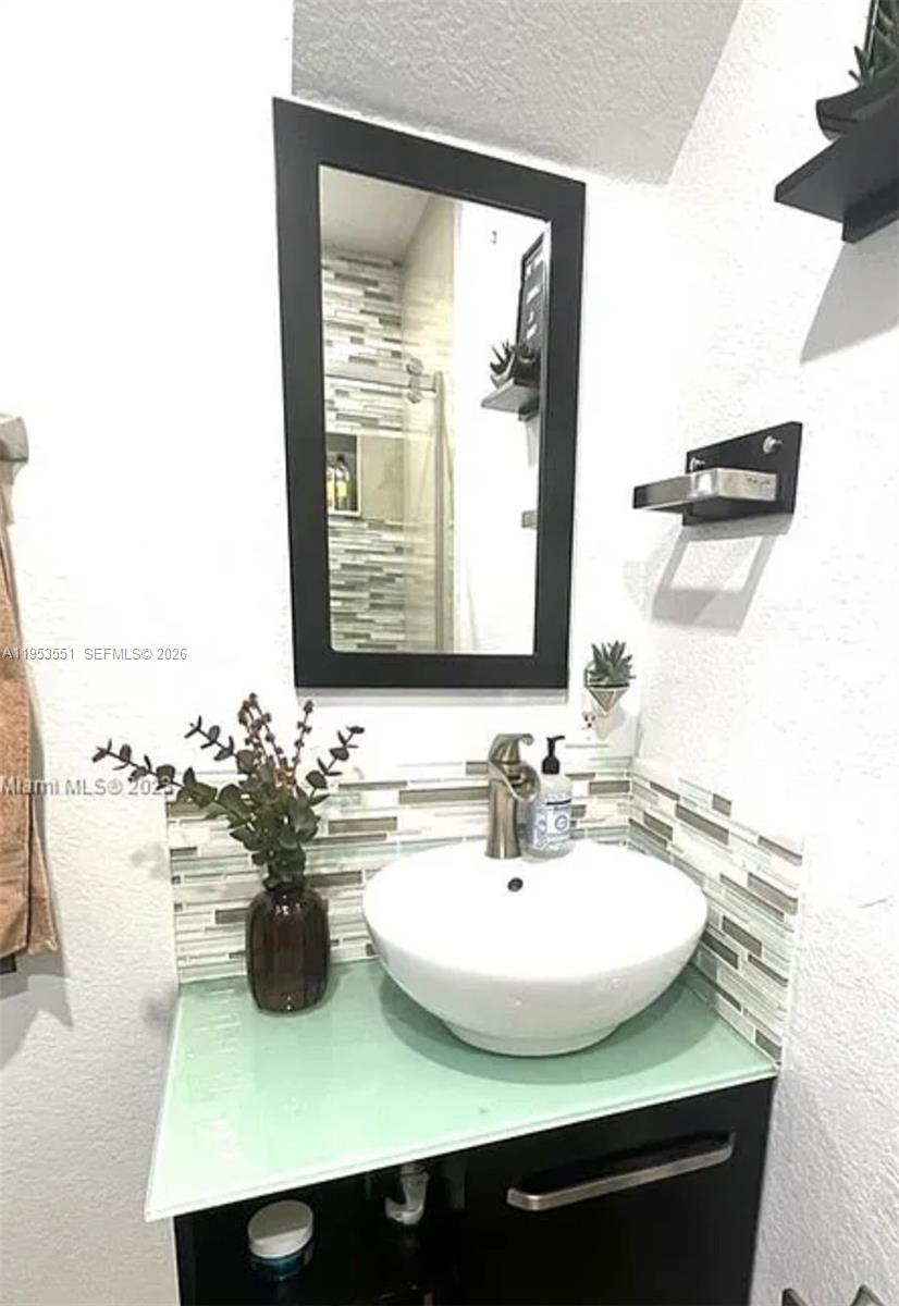 A bathroom vanity features a vessel sink, a glass countertop, and a framed mirror — 9455 NW 114th Ln # 8, Hialeah Gardens FL 33018, HIALEAH GARDENS, FL