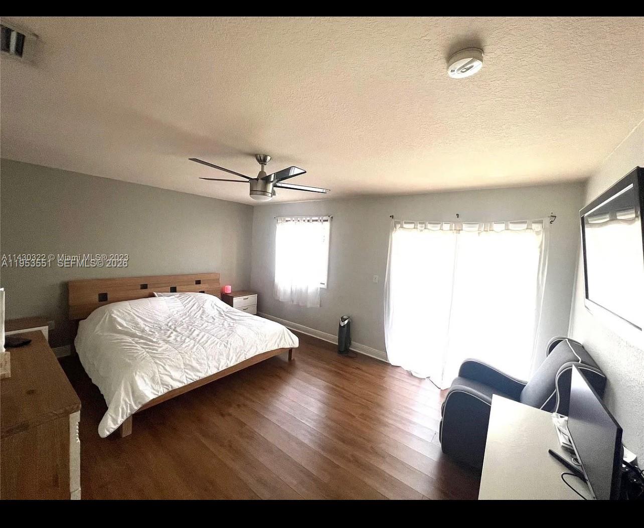 A bedroom features a wooden bed frame, wood-look flooring, a ceiling fan, and sliding glass doors — 9455 NW 114th Ln # 8, Hialeah Gardens FL 33018, HIALEAH GARDENS, FL