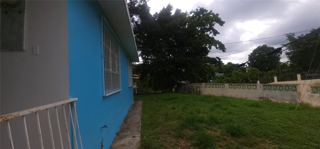A blue exterior wall of a house faces a grassy backyard with a concrete wall — Carrt. 367 Klm 0.7 BO MACHUCAL, SECTOR PAPAYO, SABANA GRANDE, PR