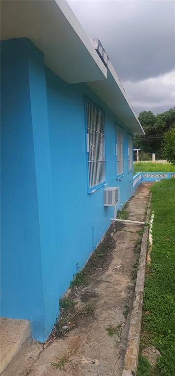 The exterior side of a bright blue house features barred windows and a concrete walkway — Carrt. 367 Klm 0.7 BO MACHUCAL, SECTOR PAPAYO, SABANA GRANDE, PR