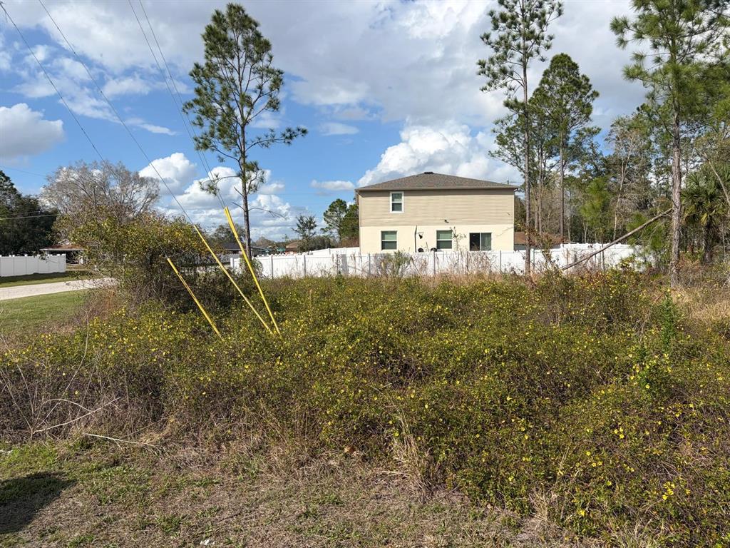 A vacant, overgrown lot sits in front of a two-story house with a white fence — 202 SPOONBILL DRIVE, POINCIANA, FL