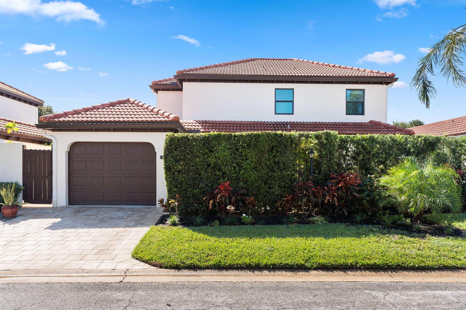 A two-story house with a brown garage door, tiled roof, and a large privacy hedge — 1484 Via Del Sol, Jupiter FL 33477, JUPITER, FL