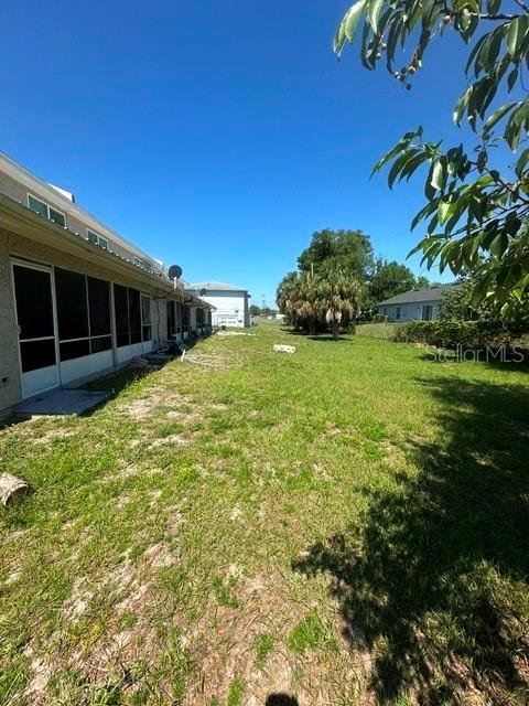 A grassy backyard area extends alongside the side of a house with a screened porch — 112 CARIBBEAN STREET, DELTONA, FL