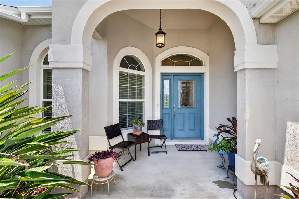 A covered front porch features a blue door, arched windows, and two black chairs — 1583 LEMON LOOP, THE VILLAGES, FL