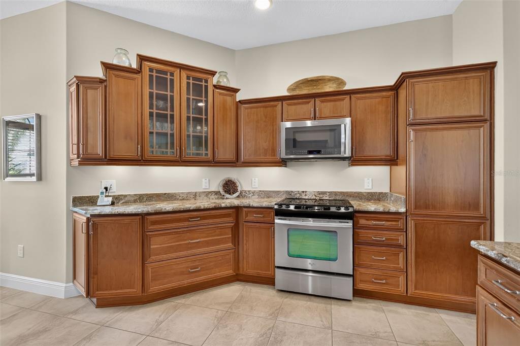 A kitchen features wood cabinets, stainless steel appliances, and granite countertops over tile flooring — 1583 LEMON LOOP, THE VILLAGES, FL
