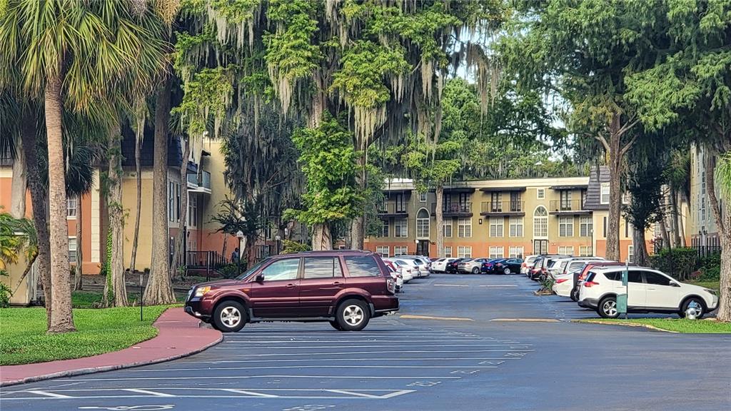 A parking lot sits in front of multi-story apartment buildings surrounded by large, mossy trees — 4023 VERSAILLES DRIVE UNIT 4023F, ORLANDO, FL