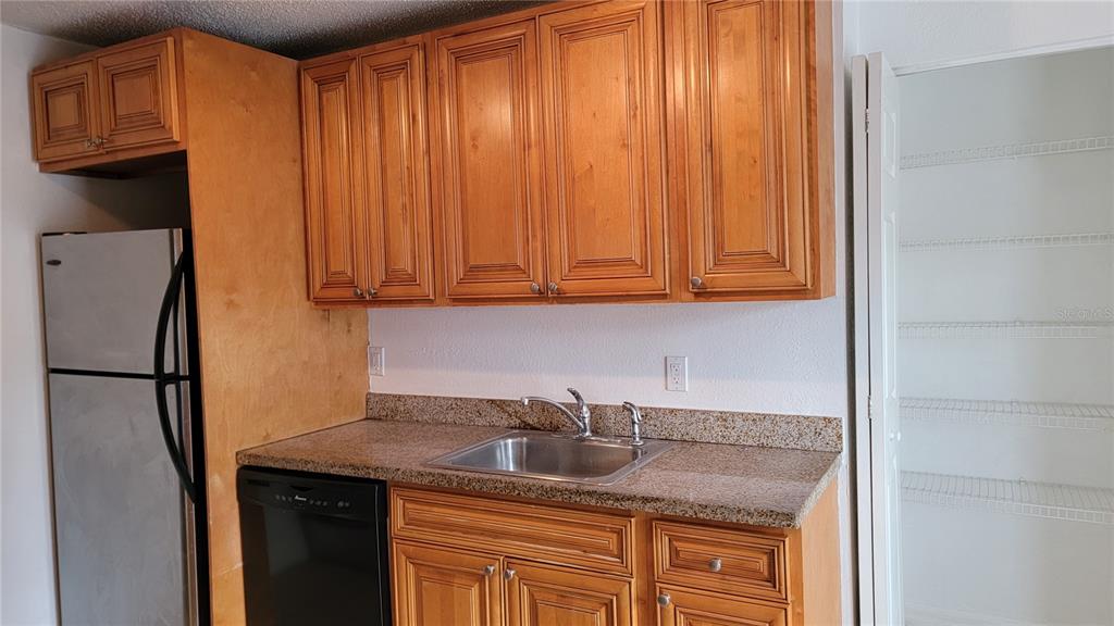 A kitchen features wood cabinets, granite countertops, a stainless steel sink, and a dishwasher — 4023 VERSAILLES DRIVE UNIT 4023F, ORLANDO, FL