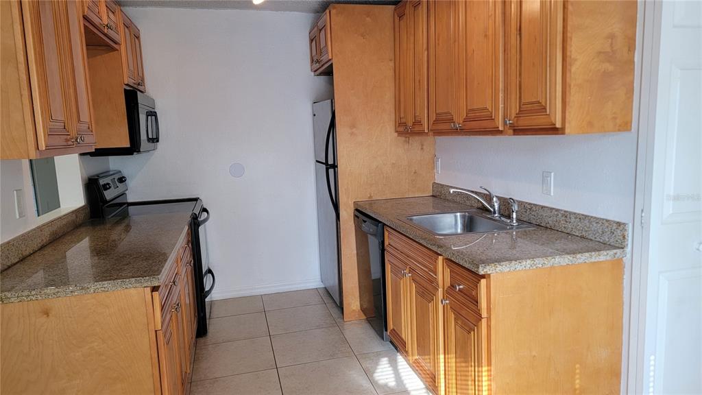 A kitchen features wood cabinets, granite countertops, stainless steel appliances, and tile flooring — 4023 VERSAILLES DRIVE UNIT 4023F, ORLANDO, FL