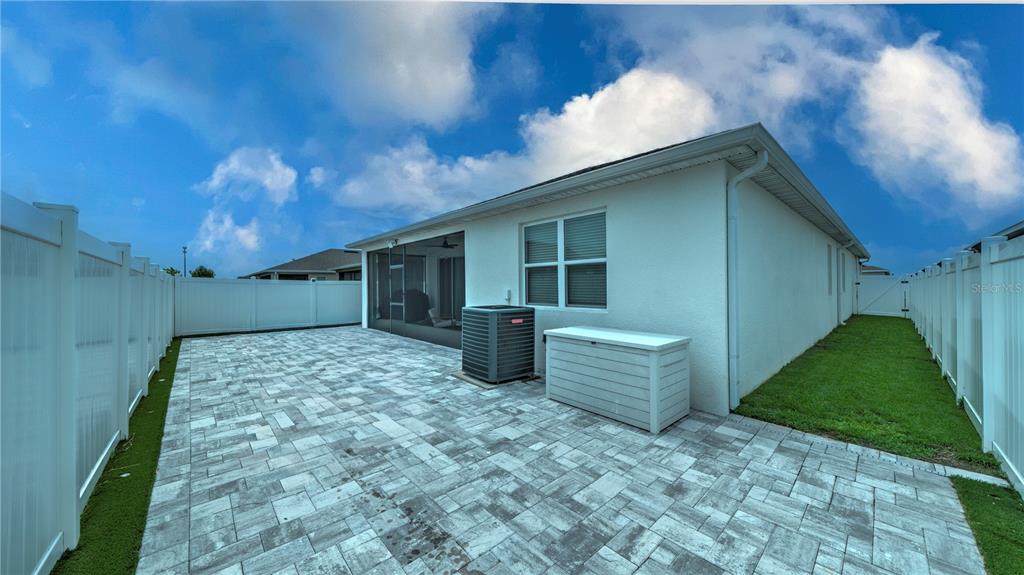 A backyard features a paved patio, a white vinyl fence, and a central air conditioning unit — 1228 MATTIE POINTE BOULEVARD, AUBURNDALE, FL