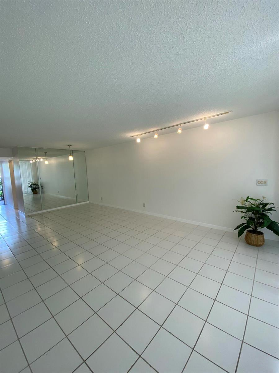 A spacious room features white tiled floors, a mirrored wall, and track lighting — 4110 Tivoli Court # 103, FL 33467, FL