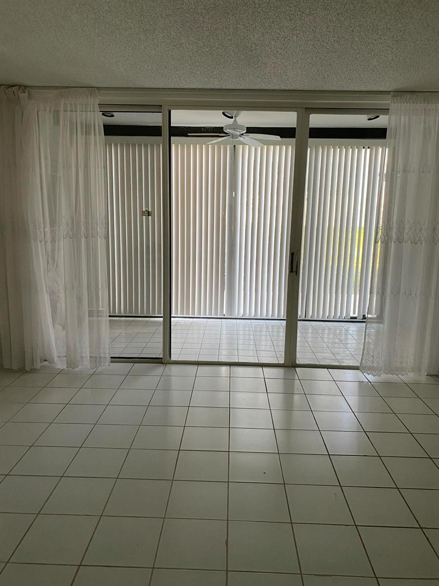 A room with white tile flooring and sliding glass doors leading to a covered balcony — 4110 Tivoli Court # 103, FL 33467, FL