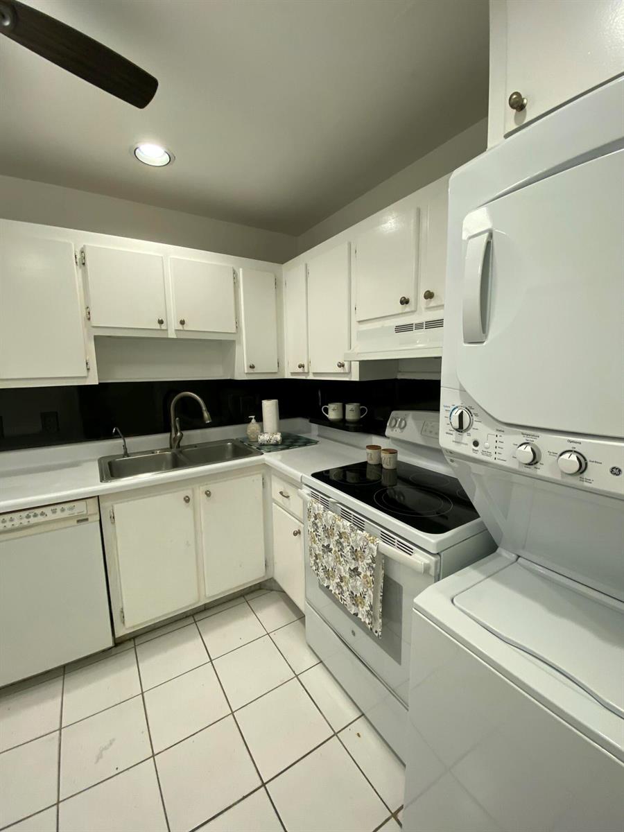A kitchen features white cabinets, a black backsplash, white appliances, and a stacked laundry unit — 4110 Tivoli Court # 103, FL 33467, FL