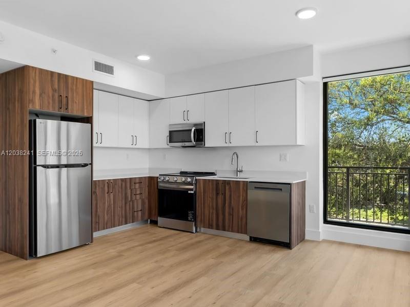 A modern kitchen features two-toned wood and white cabinetry, stainless steel appliances, and wood flooring — 2479 NE 192nd St # 308, Miami FL 33180, MIAMI, FL