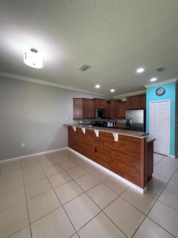 A kitchen features dark wood cabinets, a breakfast bar with wood paneling, and tile flooring — 1743 PORTOFINO MEADOWS BOULEVARD, ORLANDO, FL