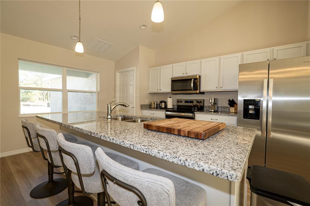 A kitchen features a granite-topped island with bar seating, white cabinets, and stainless steel appliances — 6920 SW 209TH AVENUE, DUNNELLON, FL