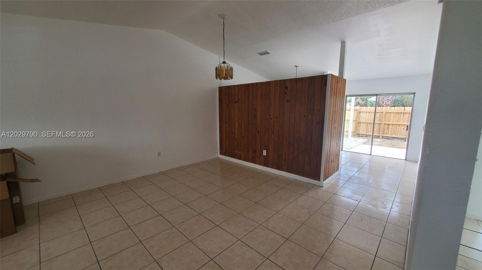 An empty room features beige tile flooring, white walls, and a wood-paneled accent wall — 18047 NW 41ST PL # 0, Miami FL 33055, MIAMI, FL