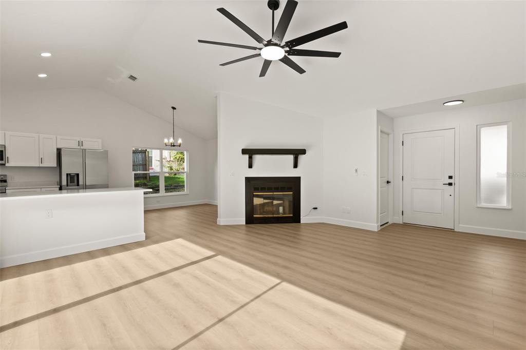 An open-concept living room and kitchen featuring light wood flooring, a fireplace, and vaulted ceilings — 7336 BORDWINE DRIVE, ORLANDO, FL