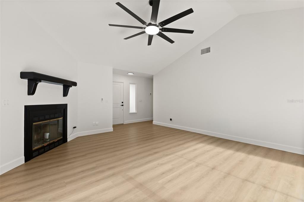 A living room with light wood flooring, a fireplace, and a vaulted ceiling with a fan — 7336 BORDWINE DRIVE, ORLANDO, FL
