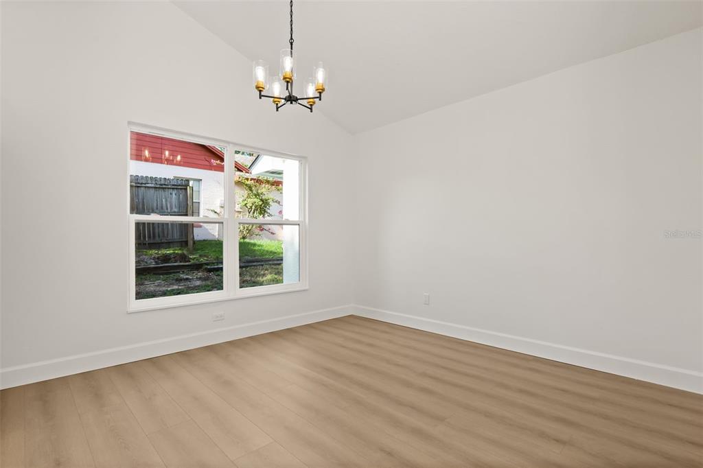 An empty room features light wood-look flooring, white walls, a vaulted ceiling, and a chandelier — 7336 BORDWINE DRIVE, ORLANDO, FL