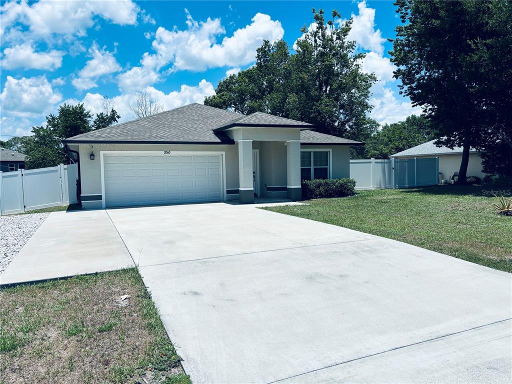 A single-story house with a two-car garage, concrete driveway, and white vinyl fencing — 2060 EVEREST STREET, DELTONA, FL