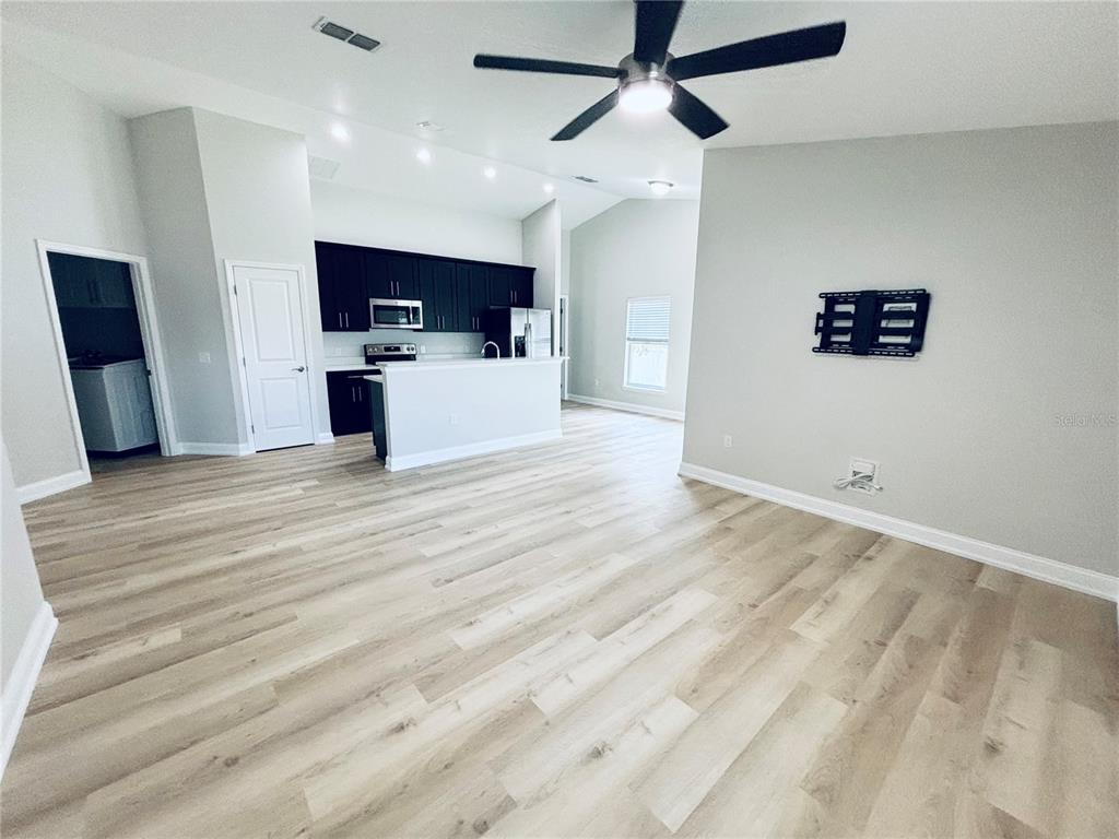 An open-concept living room features light wood-look flooring, a ceiling fan, and a dark-cabinet kitchen — 2060 EVEREST STREET, DELTONA, FL