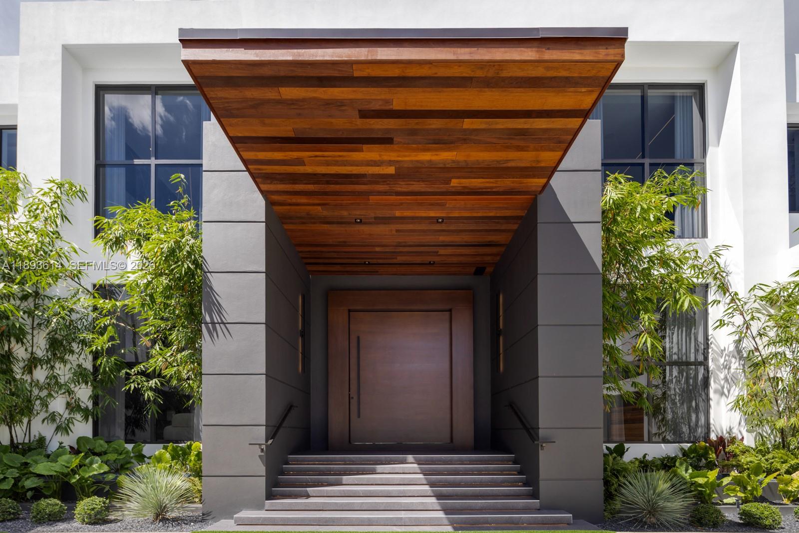 A modern home entrance features a wooden canopy, grey paneled walls, and stone steps — 9900 SW 125th Ave, Miami FL 33186, MIAMI, FL