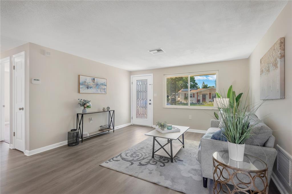 A living room features light wood-look flooring, a gray sofa, a coffee table, and a front door — 3111 COLDWELL DRIVE, HOLIDAY, FL