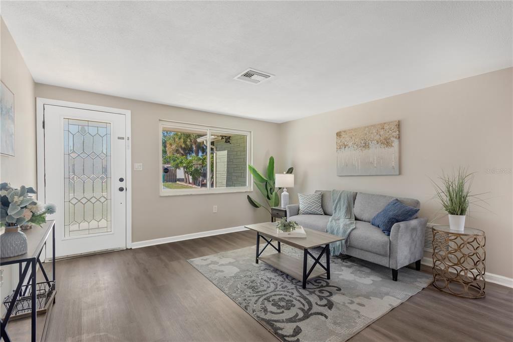 A living room features light walls, wood-look flooring, a gray sofa, and a front door — 3111 COLDWELL DRIVE, HOLIDAY, FL