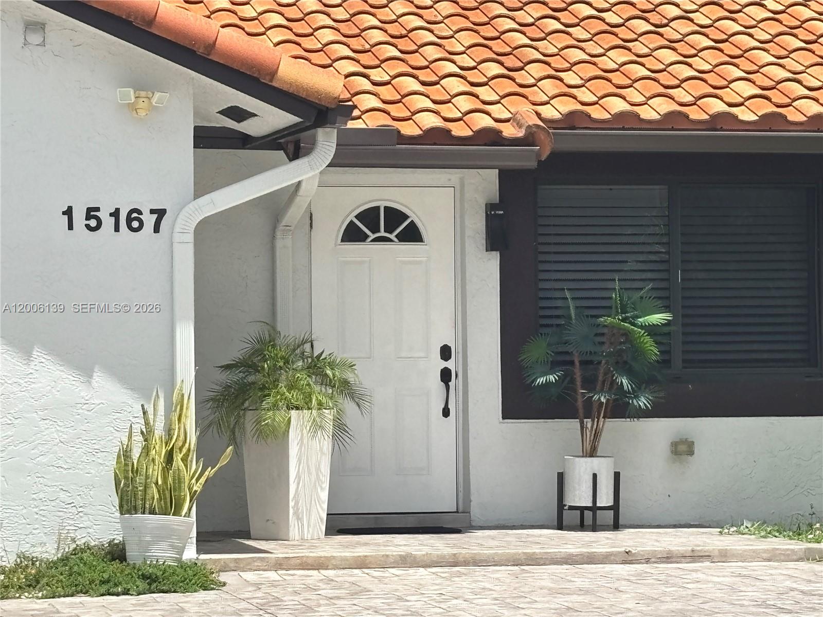 The exterior of a house features a white door, a tiled roof, and potted plants — 15167 SW 94th Ter # 1, Miami FL 33196, MIAMI, FL