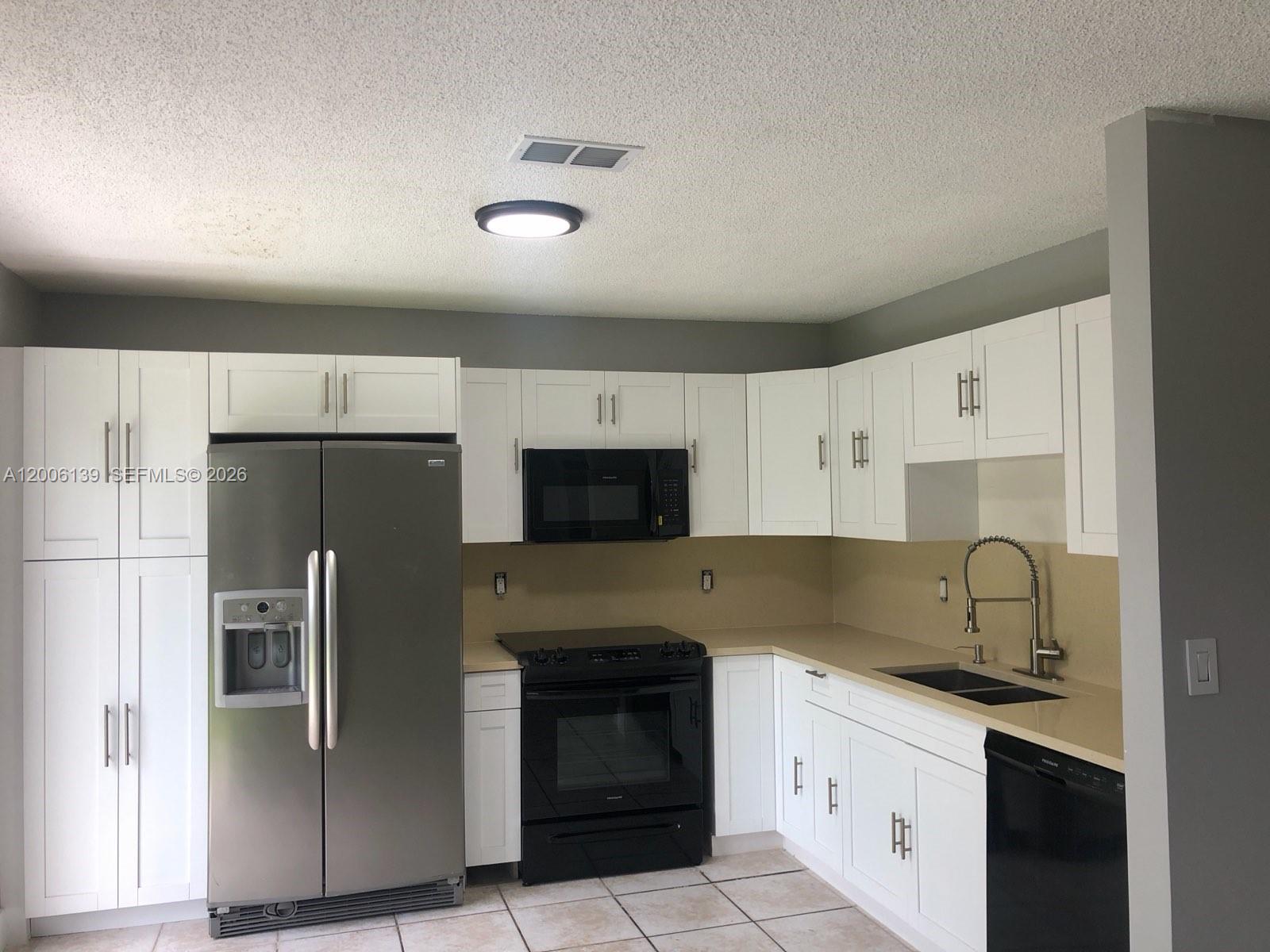A kitchen features white cabinets, stainless steel refrigerator, black appliances, and tan countertops — 15167 SW 94th Ter # 1, Miami FL 33196, MIAMI, FL