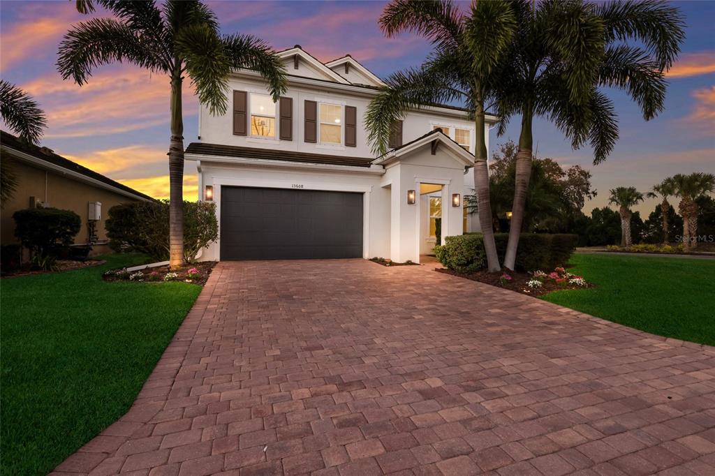 A two-story house with a paver driveway, a two-car garage, and palm trees at dusk — 13608 AMERICAN PRAIRIE PLACE, LAKEWOOD RANCH, FL