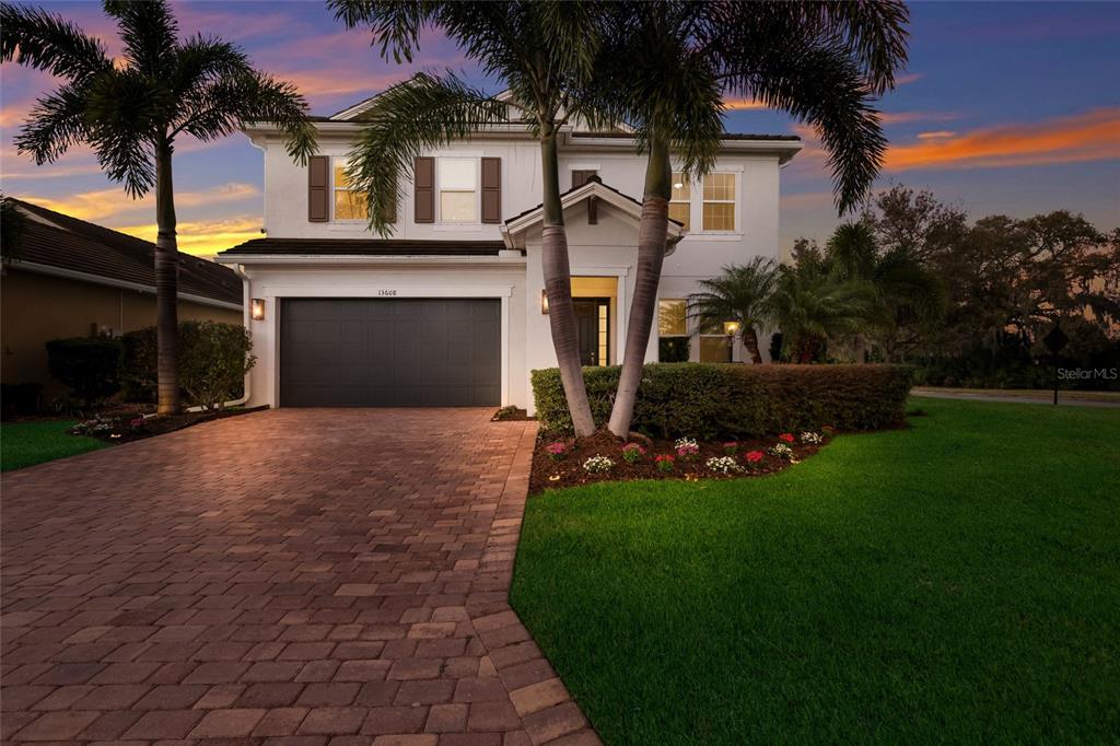 A two-story house with a paved driveway, a two-car garage, and palm trees at dusk — 13608 AMERICAN PRAIRIE PLACE, LAKEWOOD RANCH, FL