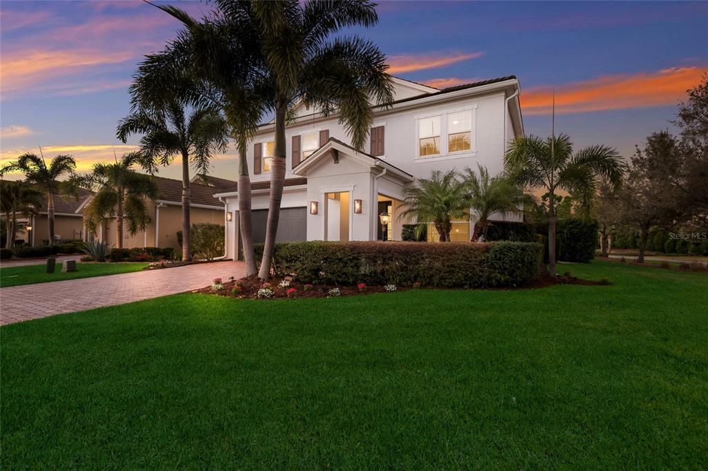 A two-story house with a paved driveway, palm trees, and a manicured lawn at sunset — 13608 AMERICAN PRAIRIE PLACE, LAKEWOOD RANCH, FL
