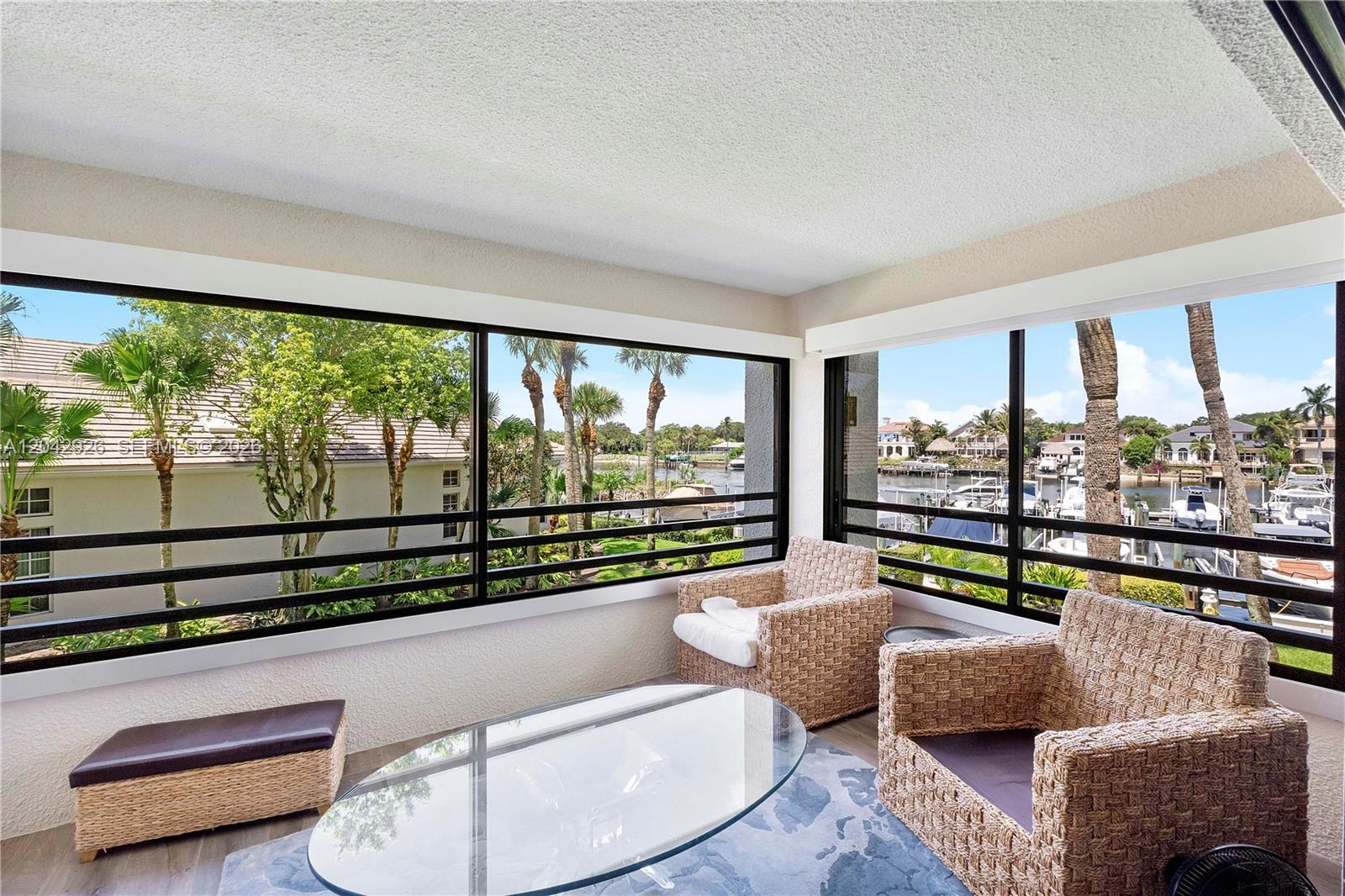 A sunroom with wicker chairs, a glass coffee table, and large windows overlooking a canal — 522 Oak Harbour Dr # 522, Juno Beach FL 33408, JUNO BEACH, FL