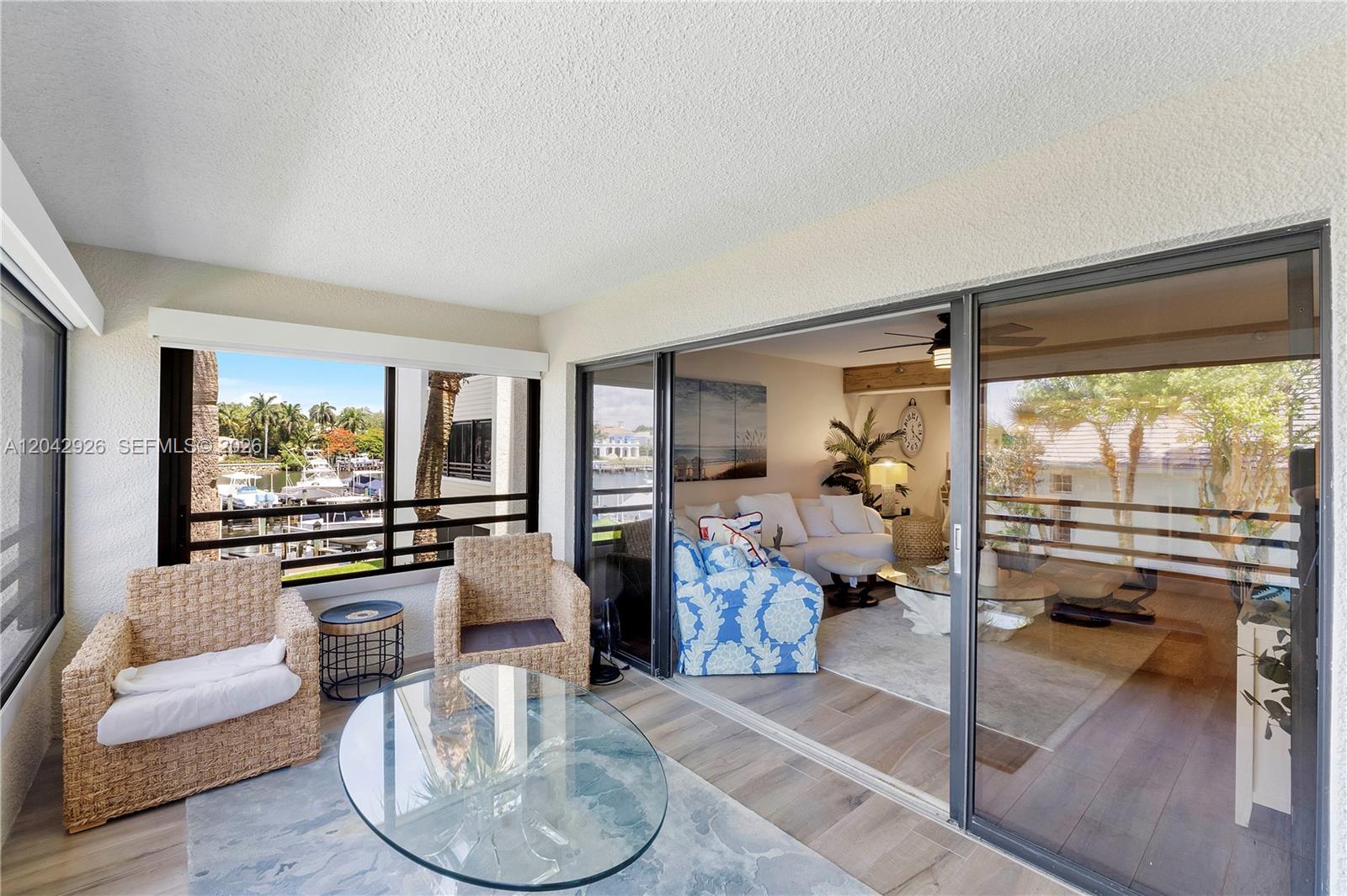 A sunroom with wicker chairs and a glass table overlooks a marina through sliding doors — 522 Oak Harbour Dr # 522, Juno Beach FL 33408, JUNO BEACH, FL
