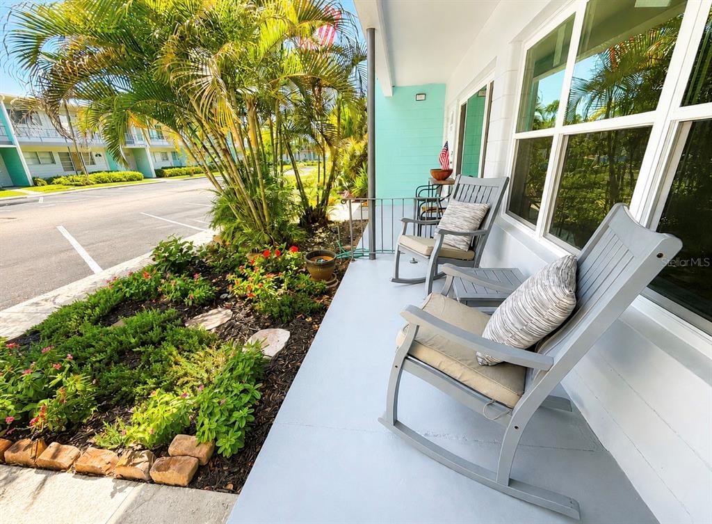 A covered porch features two gray rocking chairs and a small garden bed — 4325 58TH WAY N UNIT 1430, KENNETH CITY, FL