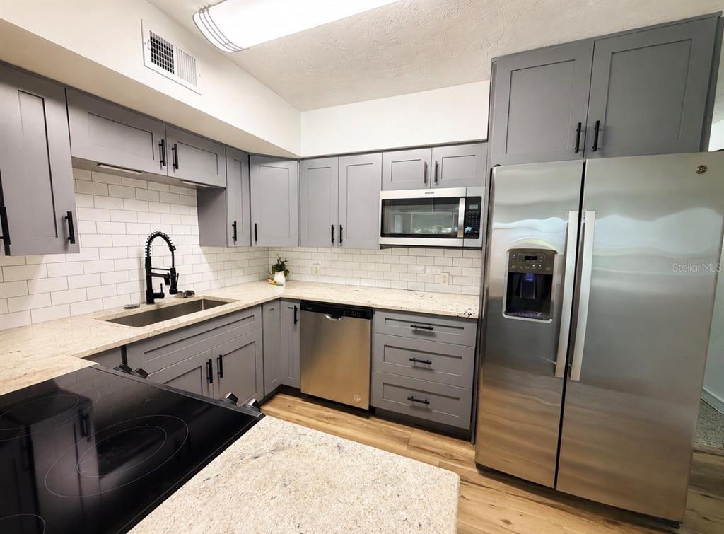 A kitchen features gray cabinets, stainless steel appliances, granite countertops, and a white subway tile backsplash — 4325 58TH WAY N UNIT 1430, KENNETH CITY, FL
