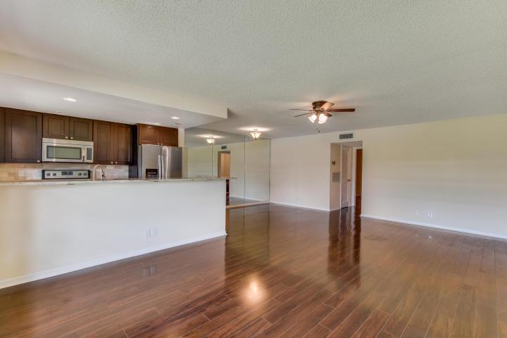 A kitchen with dark wood cabinets and stainless steel appliances overlooks a spacious living area — 797 North Drive Unit C, Delray Beach FL 33445, DELRAY BEACH, FL