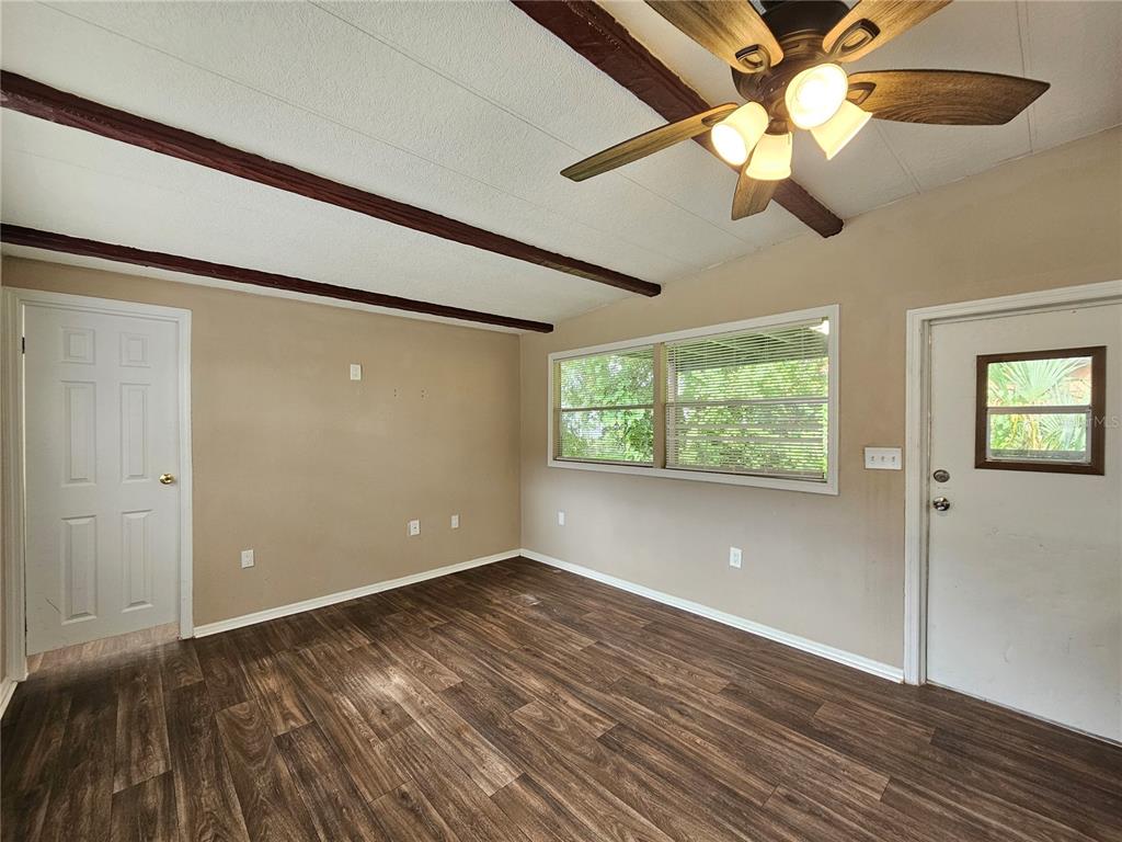 An empty room with wood-look flooring, a ceiling fan, exposed ceiling beams, and two doors — 37826 DAUGHTERY ROAD, ZEPHYRHILLS, FL