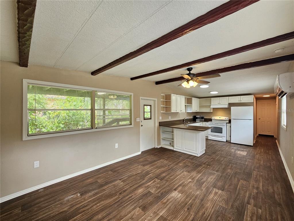 A kitchen and living area with wood-look flooring, exposed ceiling beams, and white cabinetry — 37826 DAUGHTERY ROAD, ZEPHYRHILLS, FL
