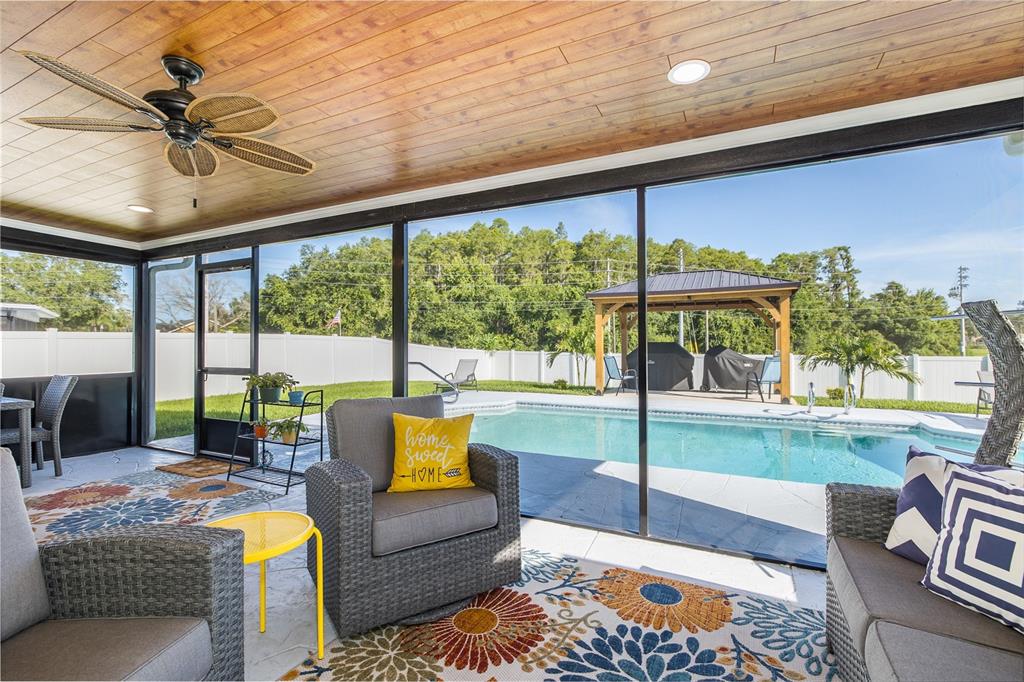 A screened-in patio features a wood-paneled ceiling, wicker furniture, and a view of a pool — 9503 CALLE ALTA, NEW PORT RICHEY, FL