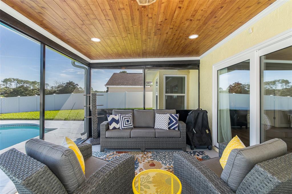 A screened-in patio features a wood-paneled ceiling, gray wicker furniture, and a backyard pool — 9503 CALLE ALTA, NEW PORT RICHEY, FL