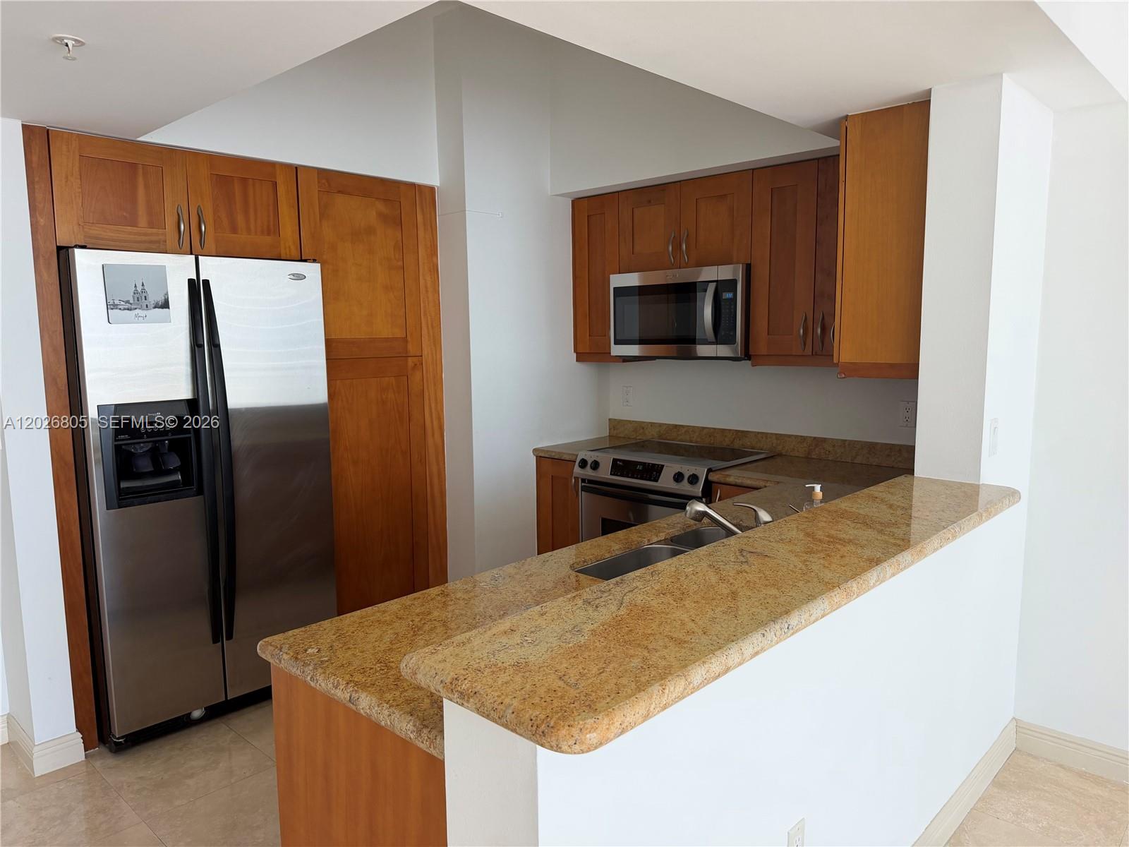 A kitchen features wood cabinets, stainless steel appliances, and a granite countertop peninsula — 1755 E Hallandale Beach Blvd # 2404E, Hallandale Beach FL 33009, HALLANDALE BEACH, FL