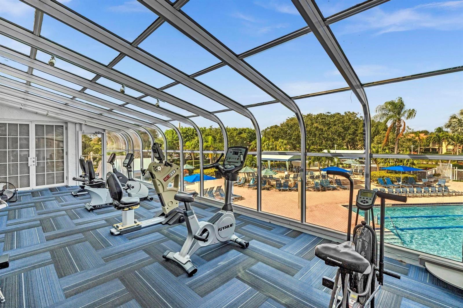 A gym with stationary exercise bikes overlooks an outdoor swimming pool through a glass enclosure — 5395 Firenze Drive # O, Boynton Beach FL 33437, BOYNTON BEACH, FL