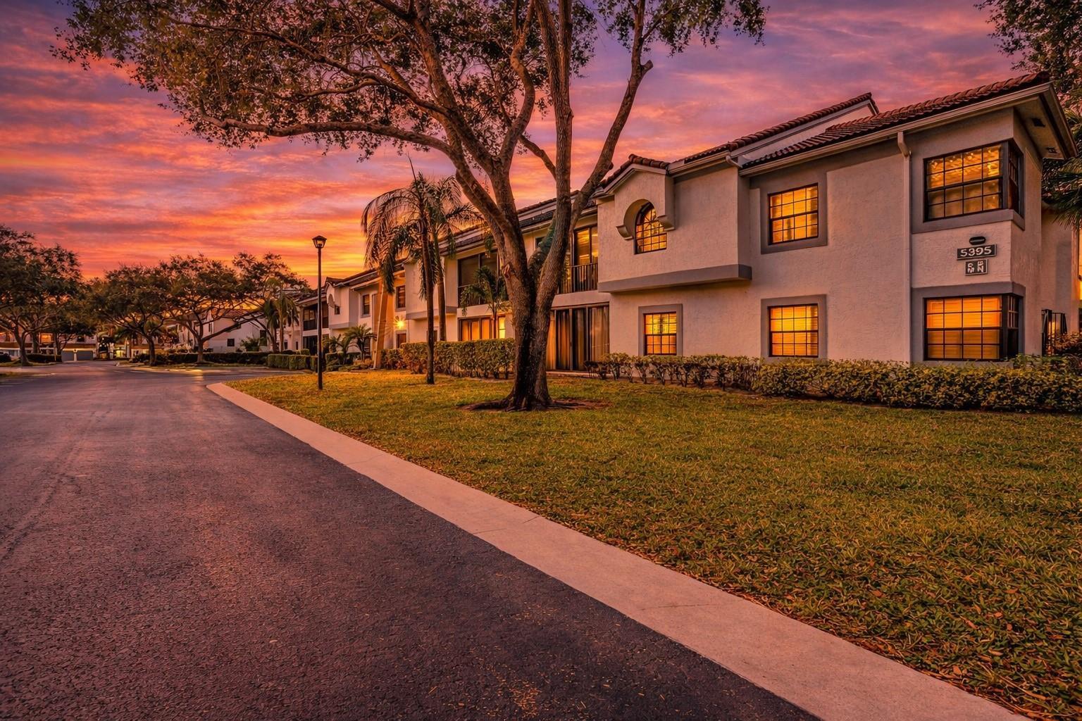 A multi-story apartment building exterior features a lawn, trees, and a sunset sky — 5395 Firenze Drive # O, Boynton Beach FL 33437, BOYNTON BEACH, FL