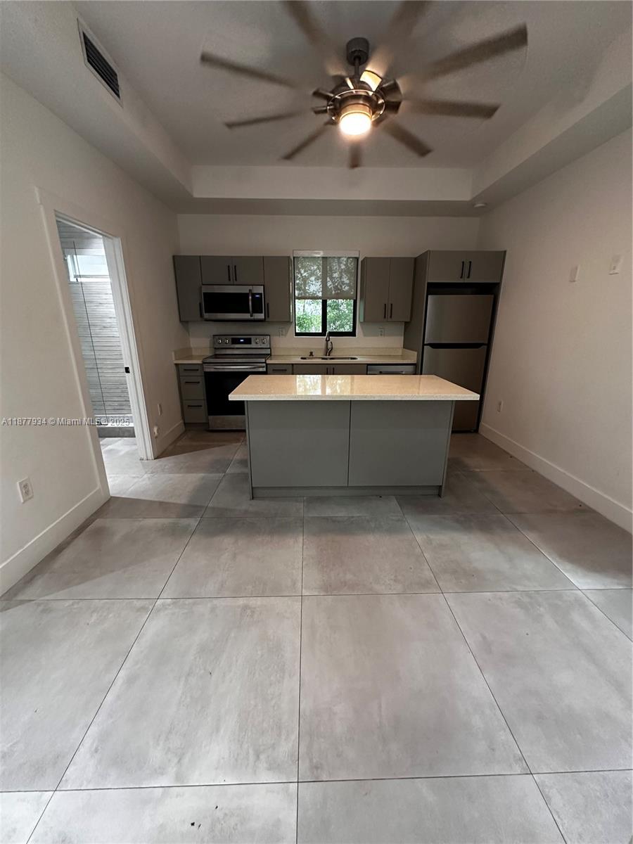 A modern kitchen features gray cabinetry, stainless steel appliances, a central island, and tiled floors — 14 Coral Dr # 1, Key Largo FL 33037, KEY LARGO, FL