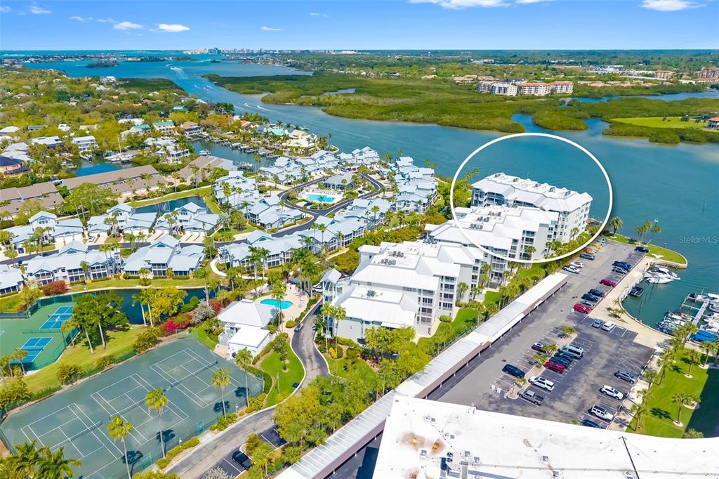 An aerial view shows a multi-story residential building complex with tennis courts and a parking lot — 1280 DOLPHIN BAY WAY UNIT 504, SARASOTA, FL