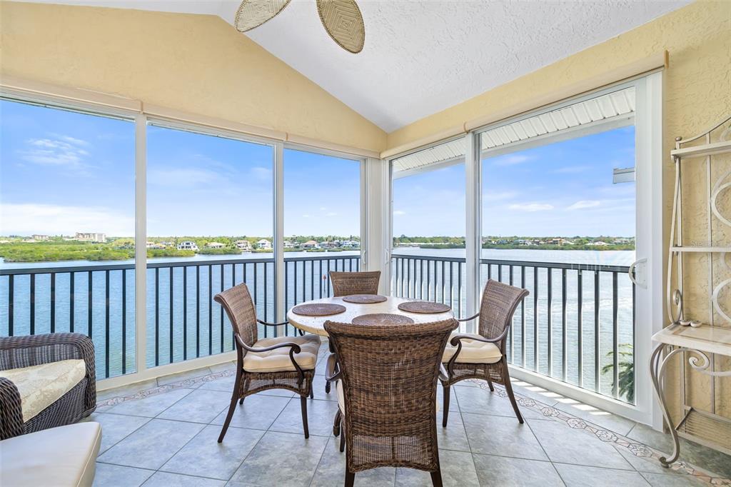 A sunroom with tile flooring and wicker furniture overlooks a body of water — 1280 DOLPHIN BAY WAY UNIT 504, SARASOTA, FL
