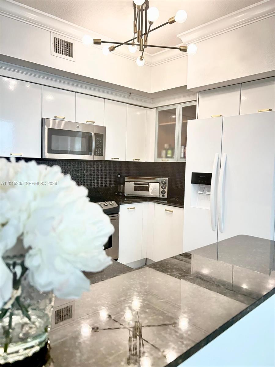 A kitchen features white cabinets, stainless steel appliances, a dark backsplash, and a modern chandelier — 625 Casa Loma Blvd # 1009, Boynton Beach FL 33435, BOYNTON BEACH, FL